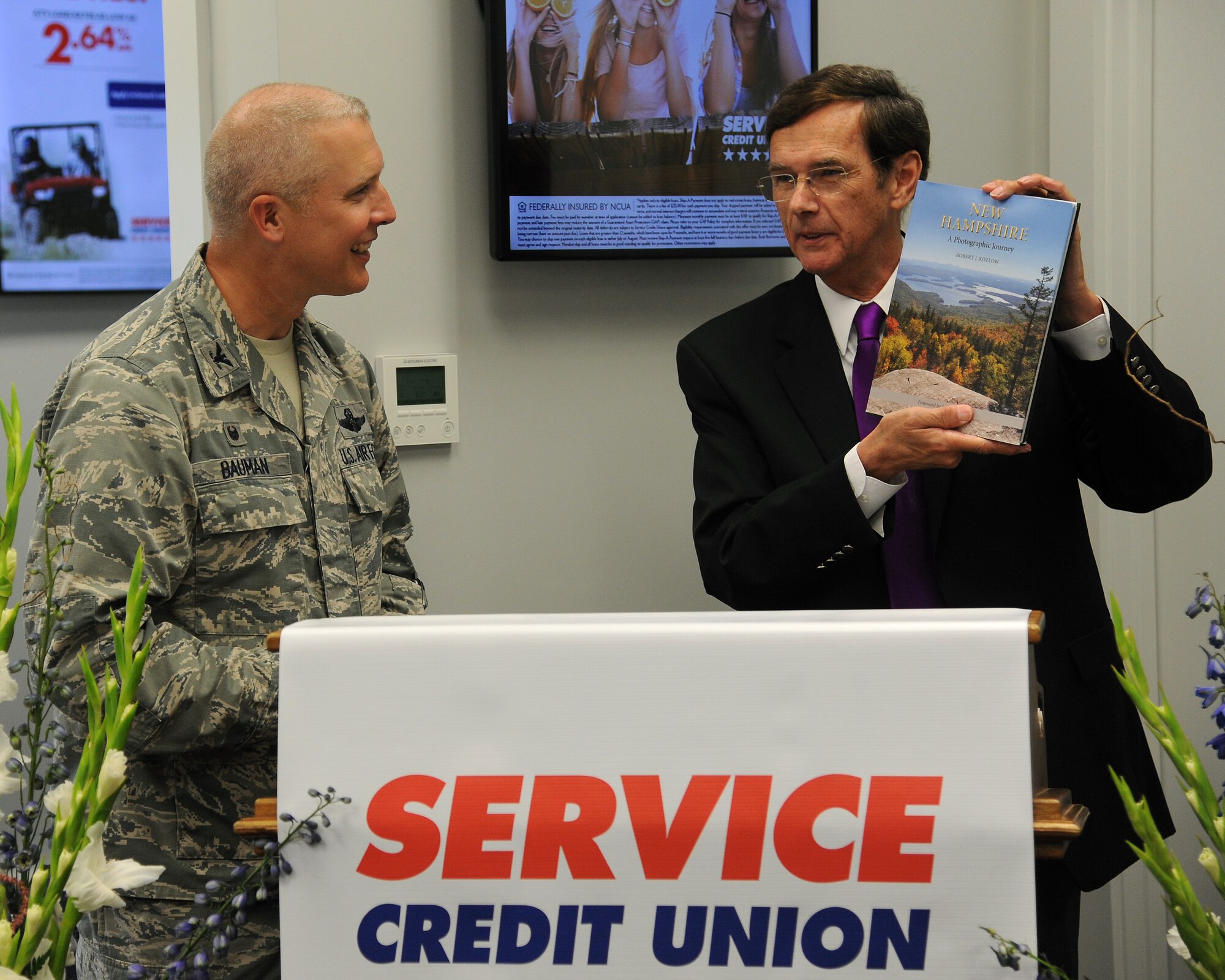 Gordon Simmons, President of Service Credit Union, presents Col. Paul Bauman, 319th Air Base Wing commander with a New Hampshire photographic journey book, comparing some pages to the North Dakota region on Grand Forks Air Force Base, N.D. on June 24, 2014. SCU was established in 1957 and has grown into a billion dollar company. (U.S. Air Force Photo by Senior Airman Zachiah Roberson/released)