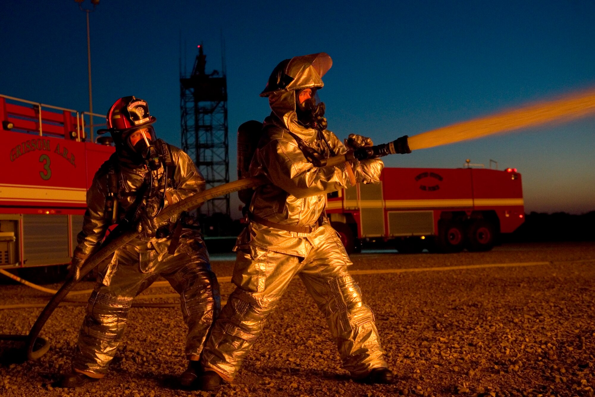 Jason Hofmeister, Grissom Fire Department firefighter, right, uses a fire hose to direct pressurized water towards a fire-engulfed mock airframe, as Capt. Jason Cahill, GFD crew chief, helps guide the fire hose during a night training exercise at Grissom Air Reserve Base, Ind. May 21, 2015. Grissom's fire pit uses propane gas to ignite the mock airframe providing firefighters a realistic training scenario.