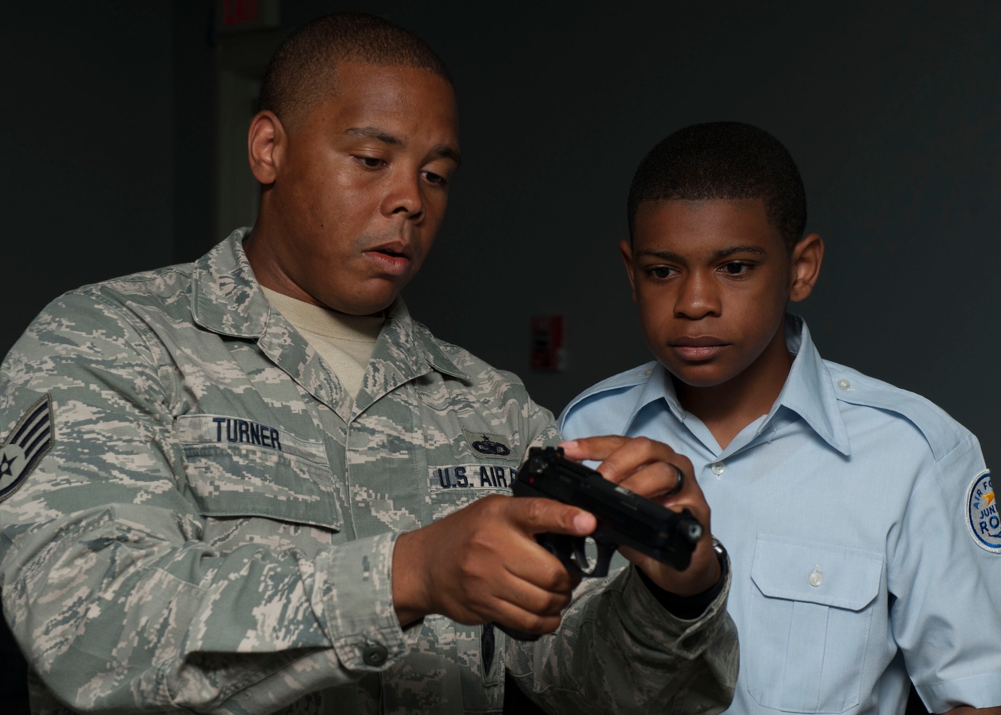 U.S. Air Force Staff Sgt. Ron Turner, 633rd Security Forces Squadron trainer, explains the safety function on the virtual range simulator’s M-9 pistol to Shahn Stewart, Nansemond River High School Junior ROTC cadet during the Shadow Day at Langley Air Force Base, Va., June 23, 2015. The cadets were given an up-close look at security forces protocols, such as use of force and weapons safety. (U.S Air Force photo by Staff Sgt. John D. Strong II/ Released)