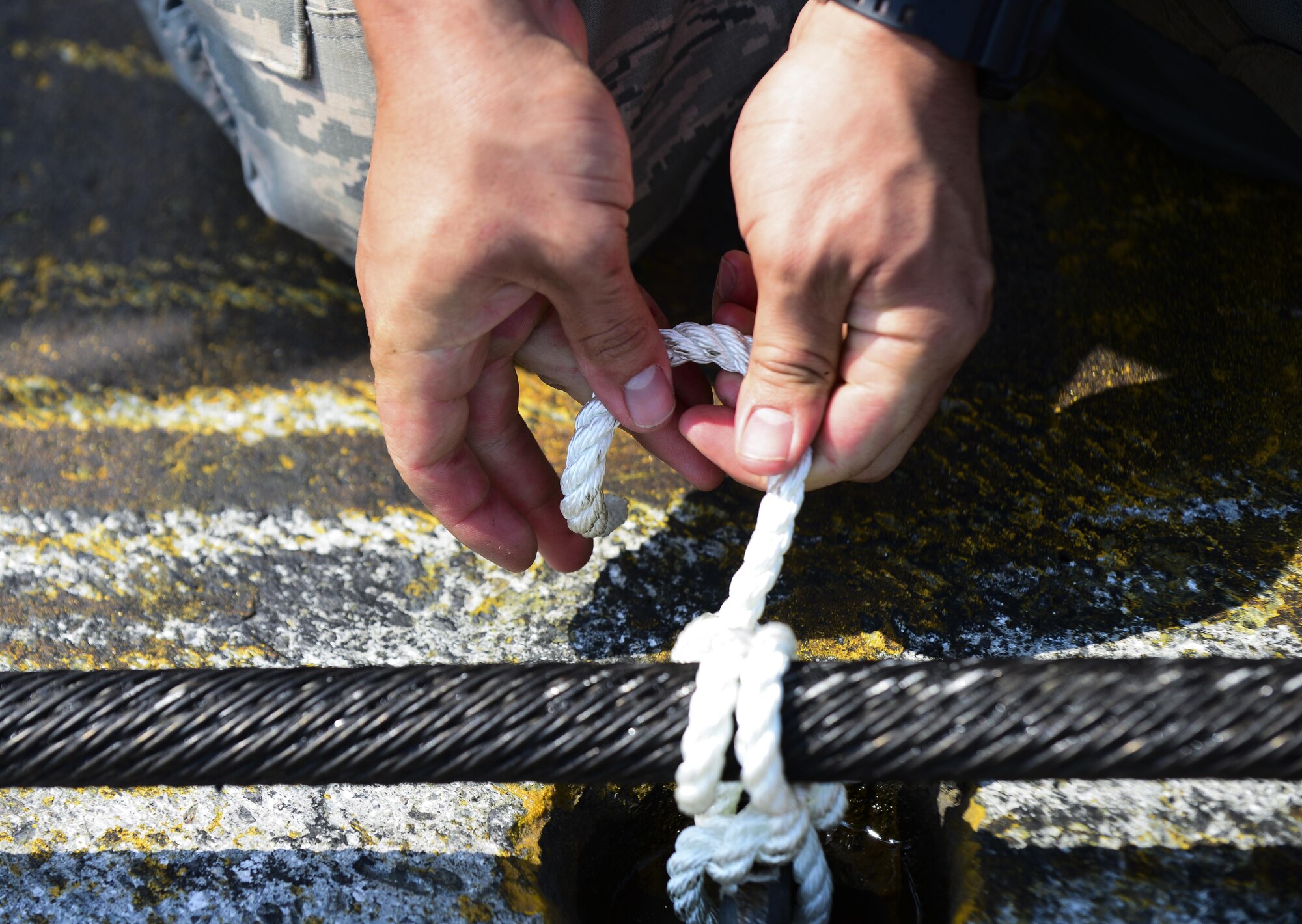 A U.S. Air Force Airman from the 374th Civil Engineer Squadron ties a knot on the aircraft arresting system at Yokota Air Base, Japan, June 24, 2015. An annual certification check's the integrity of the barriers hydraulic system and the system as a whole. (U.S. Air Force photo by Senior Airman David Owsianka/Released)