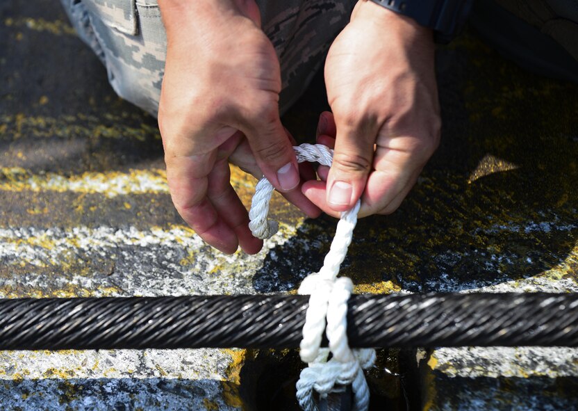 A U.S. Air Force Airman from the 374th Civil Engineer Squadron ties a knot on the aircraft arresting system at Yokota Air Base, Japan, June 24, 2015. An annual certification check's the integrity of the barriers hydraulic system and the system as a whole. (U.S. Air Force photo by Senior Airman David Owsianka/Released)