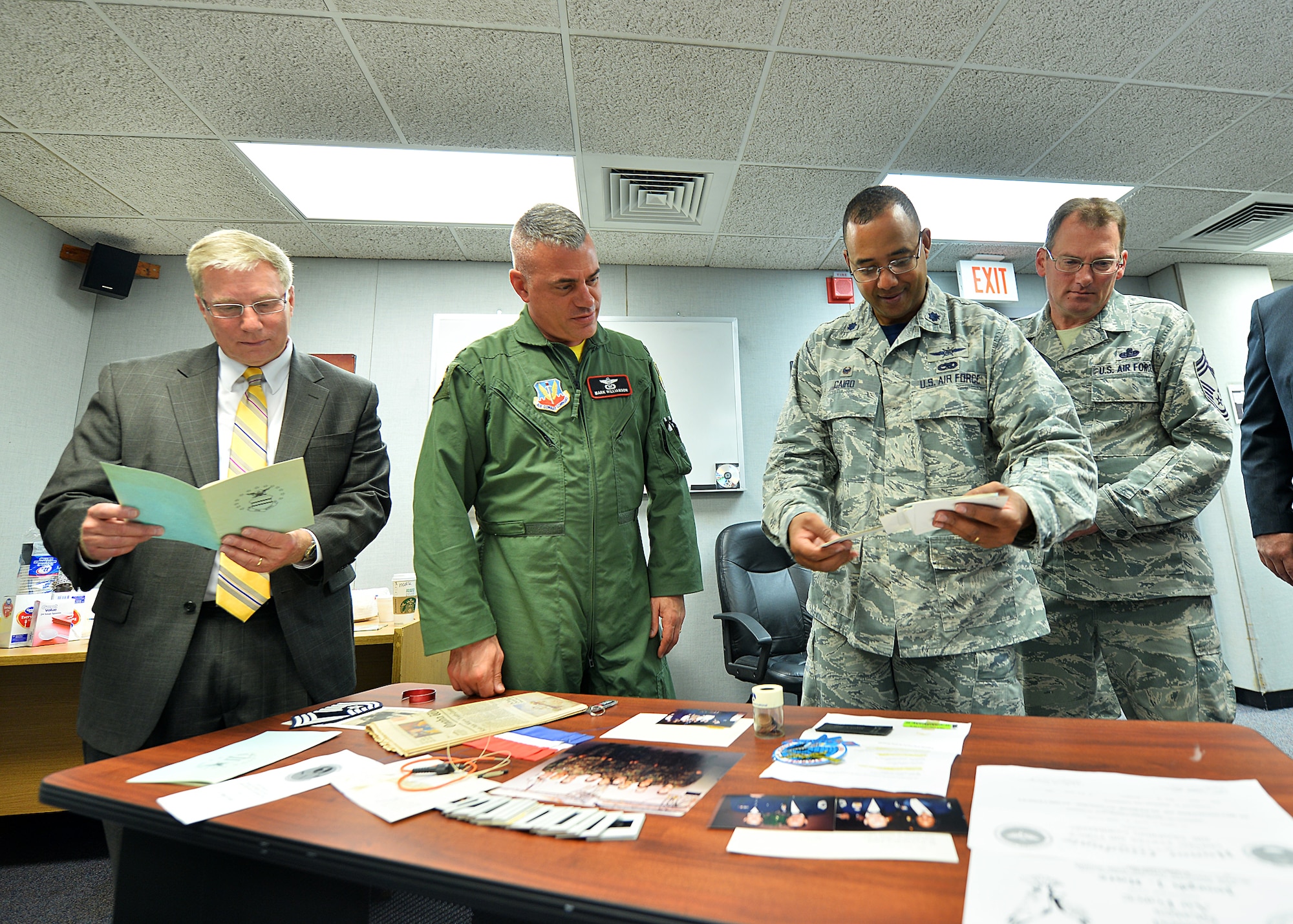 Attendees of the MILSTAR time capsule opening examine its contents June 19 at Offutt Air Force Base, Neb. Among the contents of the box were a piece of the ribbon from the ribbon cutting, a MILSTAR training certificate, local newspaper, POW/MIA bracelet, uniform name tapes, fiber optics, chief stripes and several photos. (U.S. Air Force photo by Charles Haymond/Released)