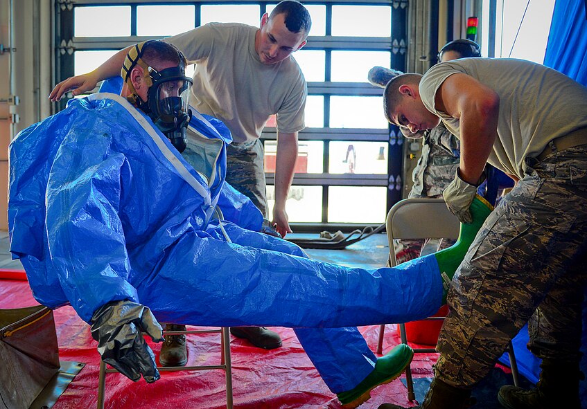 Two 6th Civil Engineering fire fighters assist in the removal of a Level A hazardous material suit from another Airman going through a HAZMAT decontamination line at MacDill Air Force Base, Fla., June 24, 2015. The decontamination line was part of a joint responder training to keep multiple agencies on base current on training requirements. (U.S. Air Force photo by Senior Airman Ned T. Johnston/Released)