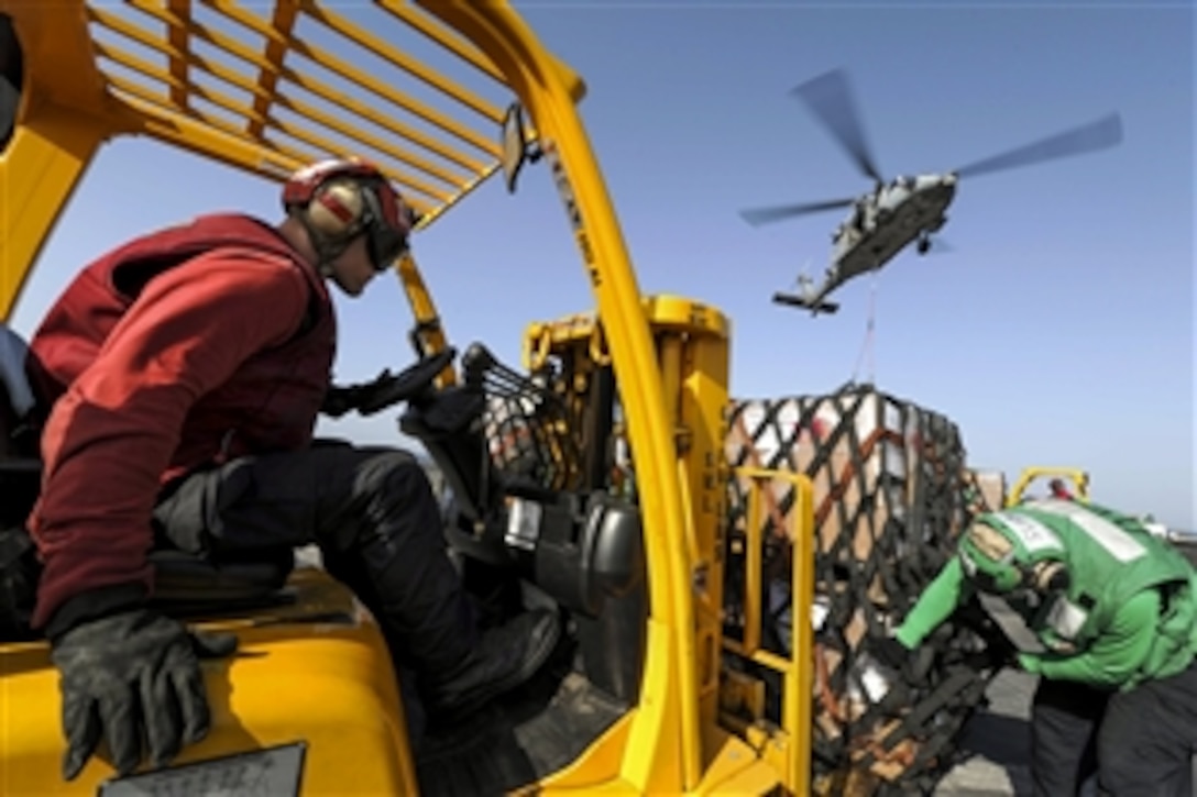 U.S. sailors move supplies on the flight deck as an MH-60 Seahawk helicopter  flies overhead aboard the aircraft carrier USS Theodore Roosevelt during a replenishment in the Arabian Gulf, June 24, 2015. The carrier is supporting Operation Inherent Resolve in the U.S. 5th Fleet area of operations. The helicopter is assigned to Helicopter Sea Combat Squadron 22.
