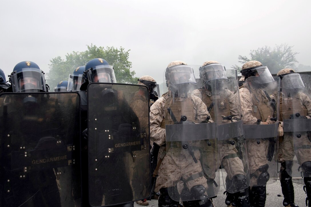 U.S. Marines with Special-Purpose Marine Air-Ground Task Force Crisis Response-Africa and members of Escadron de Gendarmerie Mobile, a unit with France’s force known as the Gendarmerie, stand shoulder to shoulder to protect against rioters at the National Gendarmerie Training Center in St. Astier, France, June 19, 2015. The two groups provided mutual support as they maneuvered their formations to protect strategic security points.  (U.S. Marine Corps photo by 1st Lt. Danielle Dixon/Released)