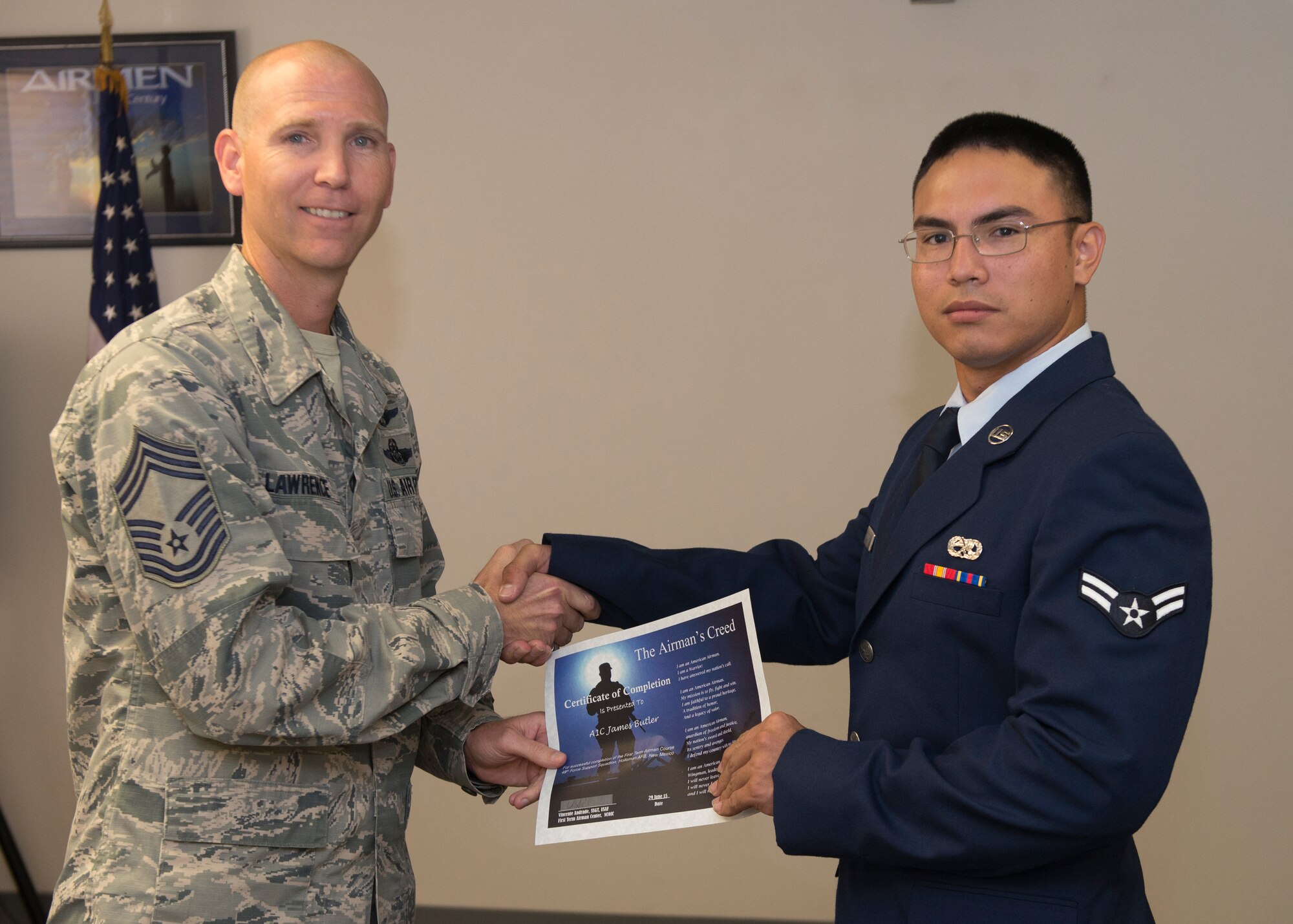 Chief Master Sgt. Gary Lawrence, 49th Operations Group chief enlisted manager presents Airman 1st Class James Butler with a First Term Airman Course graduation certificate at Holloman Air Force Base, N.M., June 29, 2015. FTAC is a program that helps first term Airmen with the transition from technical school to an operational environment. It also gives the Airmen a warm welcome to Holloman from the majority of base agencies they will be working with on a daily basis. (U.S. Air Force photo by Senior Airman Aaron Montoya / Released)