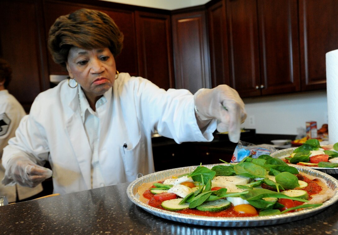 Bessie Powers, Healthy Cooking Made Easy volunteer culinary specialist, adds final topping to pizza during a healthy cooking demonstration at Liberty Park Welcome Center on Joint Base Andrews, Md., June 25, 2015. The Health Promotion office teamed up with Air Force District of Washington enlisted aides to teach more than 30 service members and their families how to prepare healthy meals. (U.S. Air Force photo/ Staff Sgt. Nichelle Anderson)