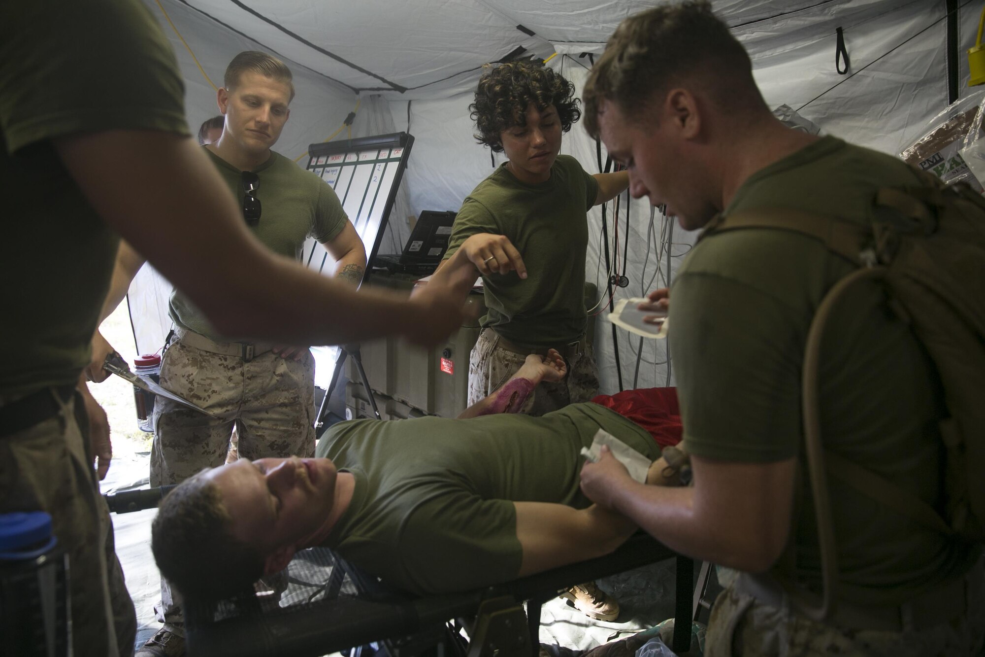 Sailors with 2nd Medical Battalion, 2nd Marine Logistics Group, assess simulated injuries on a role player, June 23, 2015, aboard Camp Lejeune, N.C., as part of a field exercise. The patient suffered an arm laceration, which required the corpsmen and doctors to pack the wound and cover it with a pressure bandage. The medical exercise is being conducted in order to familiarize the medical personnel with their capabilities and equipment in an austere environment before future missions. (U.S. Marine Corps photo by Cpl. Elizabeth Case/Released)