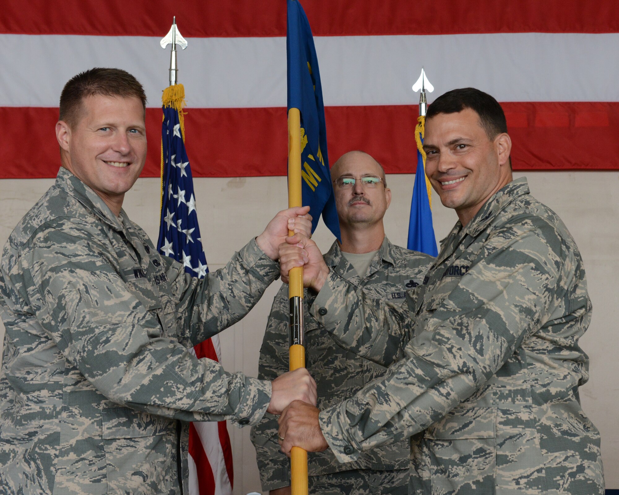 U.S. Air Force Col. Michael Winkler, the 354th Fighter Wing commander, passes the 354th Maintenance Group guidon to Col. Greg Hutson, the new 354th MXG commander, June 30, 2015, at Eielson Air Force Base, Alaska. Lt. Col. Bart Kenerson, the outgoing group commander, will move on to Langley Air Force Base, Va. (U.S. Air Force photo by Senior Airman Ashley Nicole Taylor/Released)
