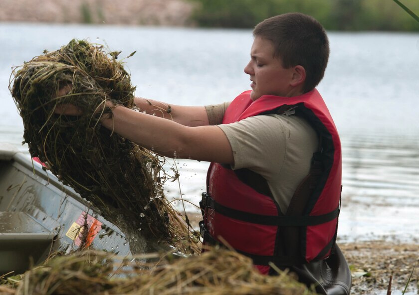 Airman 1st Class Melissa Waszkiewicz, 28th Civil Engineer Squadron pest management technician, throws weeds into a boat at Gateway Lake at Ellsworth Air Force Base, S.D., June 24, 2015. The pest management flight’s mission prevents pests and diseases from adversely affecting military operations in peacetime and during contingency operations. (U.S. Air Force Photo by Airman Sadie Colbert/Released)