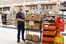 Jerry Contreras, Commissary store director, poses next to a rack of custom-made donation bags June 29 developed for the Feds Feeds Families program at Malmstrom Air Force Base’s Commissary. The Commissary serves as the base’s FFF headquarters where donations are collected and picked up by local food banks. (U.S. Air Force photo/Airman 1st Class Collin Schmidt) 