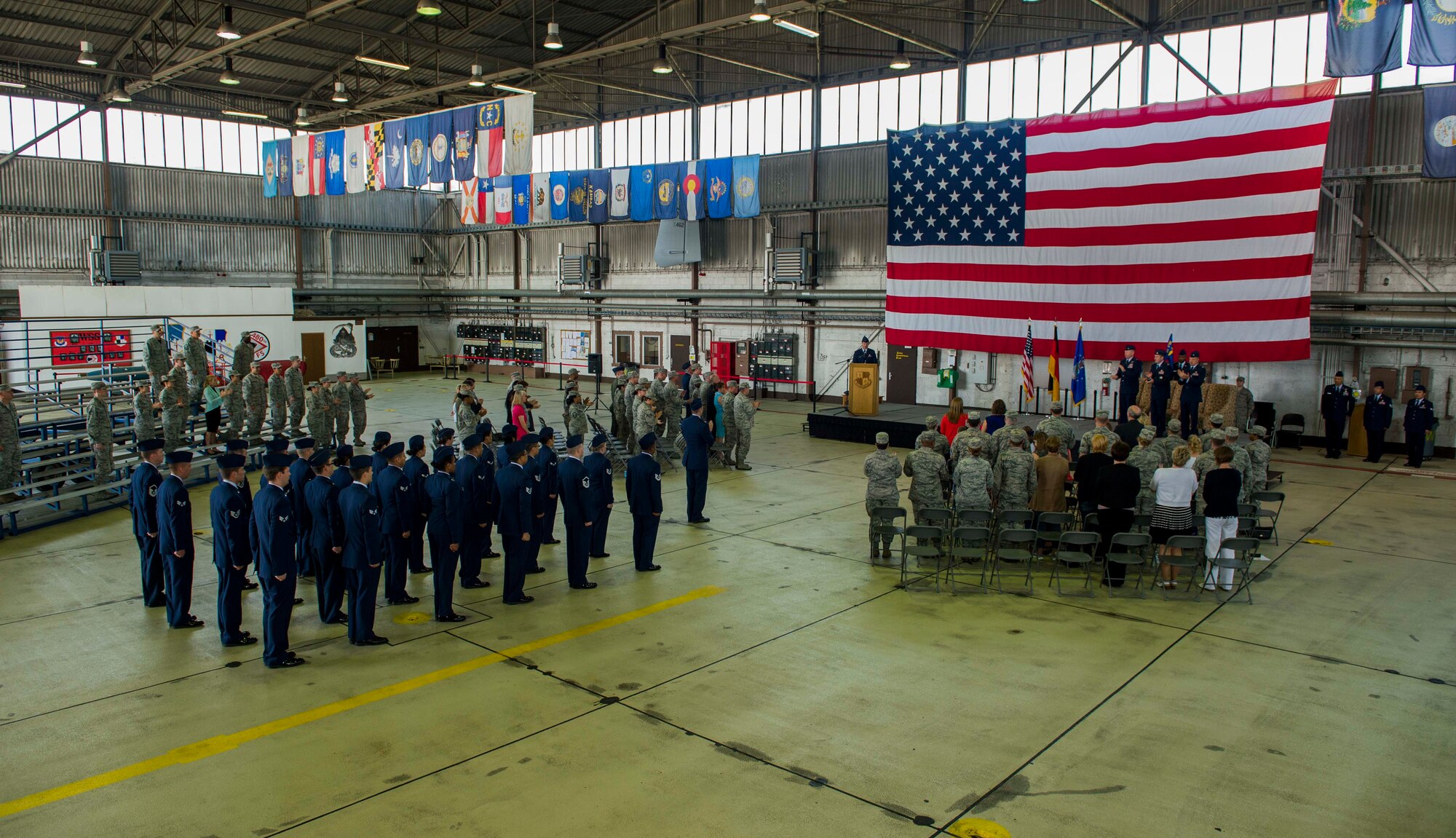 Members of the Spangdahlem community stand for the singing of the Air Force Song at the end of the 52nd CPTS change of command ceremony in Hangar One on Spangdahlem Air Base, Germany, June 26, 2015. The change of command is a military tradition that represents a formal transfer of authority and responsibility for a unit from one leader to another. (U.S. Air Force photo by Airman 1st Class Timothy Kim/Released)
