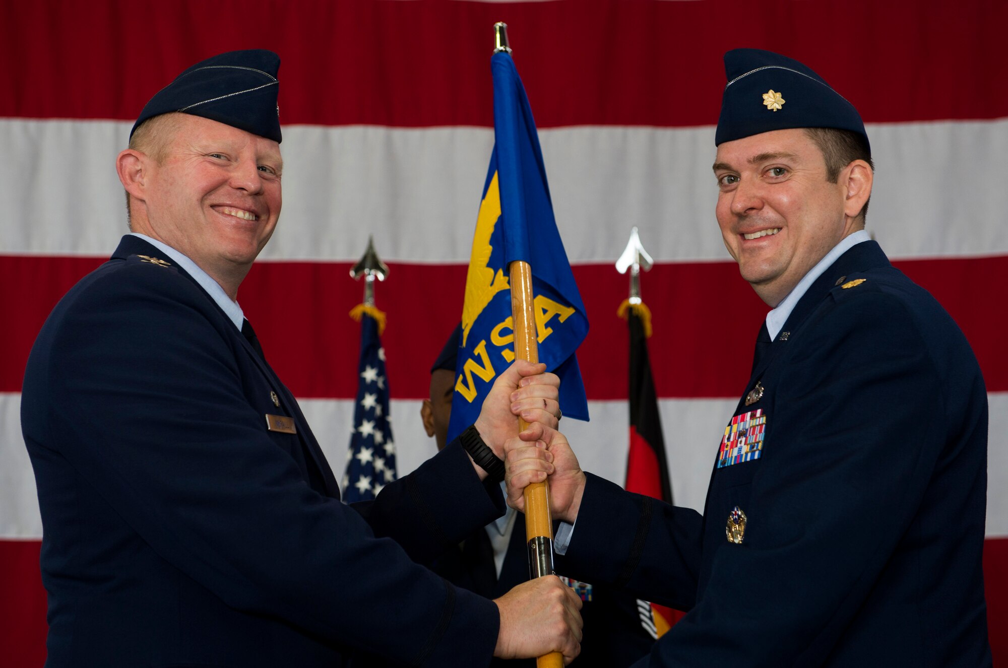 U.S. Air Force Col. Joe McFall, 52nd Fighter Wing commander, left, hands the ceremonial guidon to U.S. Air Force Maj. Neil Harris, the incoming 52nd Comptroller Squadron commander, during the 52nd CPTS change of command ceremony in Hangar One on Spangdahlem Air Base, Germany, June 26, 2015. Harris assumed command from former commander, U.S. Air Force Richard Atwell. (U.S. Air Force photo by Airman 1st Class Timothy Kim/Released)