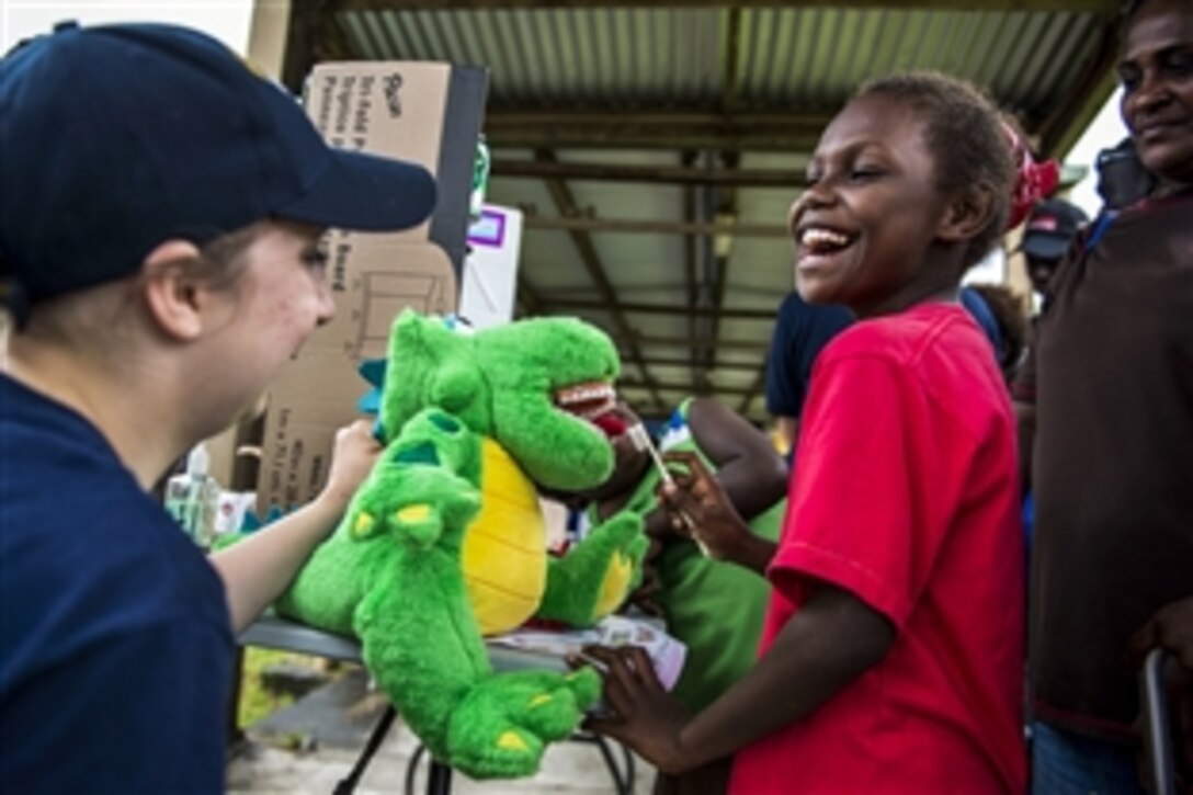 U.S. Navy Seaman Lyric Peterson helps a child practice dental hygiene on a toy dinosaur during a Pacific Partnership 2015 community health engagement at a clinic in Arawa, Papua New Guinea, June 29, 2015. Medical personnel from the hospital ship USNS Mercy visited the clinic to provide residents with medical services and information.