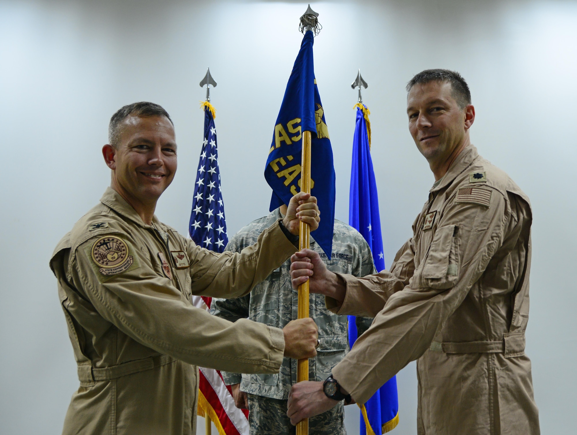 U.S. Air Force Col. Jim Dittus, left, 379th Expeditionary Operations Group commander, passes the 746th Expeditionary Airlift squadron guidon to Lt. Col. Byron Newell during a change of command ceremony, March 1, 2015 at Al Udeid Air Base, Qatar. Newell assumed command of the 746th EAS from Lt. Col. Jeremy Schaad. (U.S. Air Force photo by Senior Airman Kia Atkins)