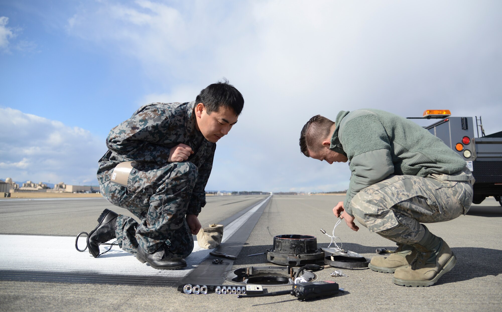 Japan Air-Self Defense Force Staff Sgt. Shinya Kobayashi, 1st Missile Group electrician, and Air Force Senior Airman Scott Armstrong III, 374th Civil Engineer Squadron electrical systems technician, inspect the inner workings of a flightline centerline light during the noncommissioned officer exchange program at Yokota Air Base, Japan, Feb. 20, 2015. Twenty-four individuals consisting of JASDF and U.S. members participated in the exchange. (U.S. Air Force photo by Senior Airman Michael Washburn/Released)