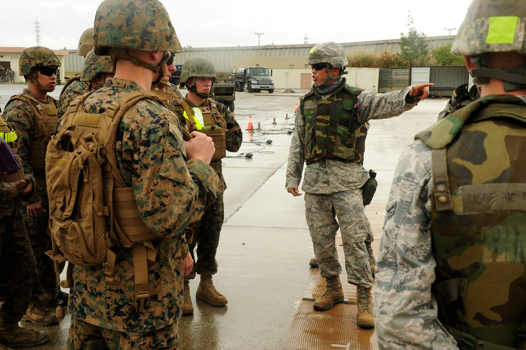 U.S. Air Force Tech. Sgt. Giles Dame, 18th Civil Engineer Squadron Structures Shop NCO in charge, speaks to Airman and Marines at Kadena Air Base, Japan Feb. 26, 2015. Dame explained what specifications are needed to secure a folded fiber glass mat over a crater during a joint airfield damage and repair contingency exercise. (U.S. Air Force photo by Airman 1st Class John Linzmeier)