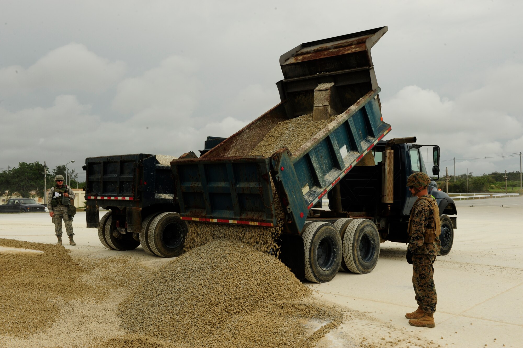 An Airman and Marine spot a dump truck as it unloads crushed stone onto a mock runway during a joint airfield damage and repair contingency exercise at Kadena Air Base, Japan Feb. 26, 2015.  Civil engineer Airmen and Marines from the 172nd and 171st Engineering Companies worked together to repair a 50 foot crater to test and improve their effectiveness at reestablishing an operational runway. (U.S. Air Force photo by Airman 1st Class John Linzmeier)