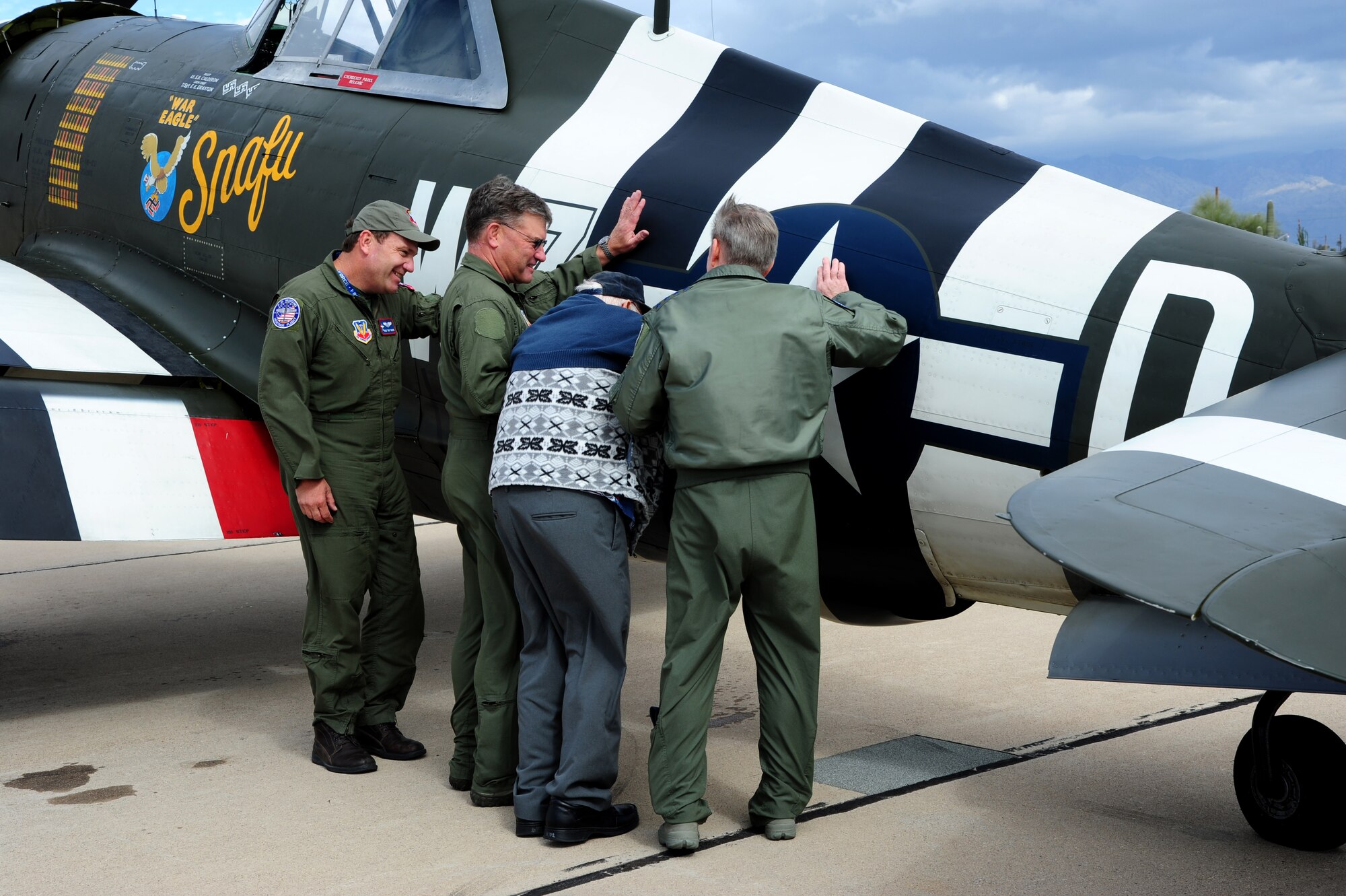 (Center) Retired Chief Warrant Officer 2 Robert Hertel, 92-year-old World War II veteran, places his hand on the side of a P-47 Thunderbolt for the first time in years with the assistance of Charles Hainline, Tom Gregory, both P-47 Thunderbolt Heritage Flight pilots, and U.S. Air Force General Hawk Carlisle, Commander of Air Combat Command, at Davis-Monthan Air Force Base, Ariz., Feb. 28, 2015. Hertel was given the opportunity to visit the aircraft he flew during WWII, up-close and personal, during the 2015 Heritage Flight Training and Certification Course. (U.S. Air Force Photo by Staff Sgt. Courtney Richardson)
