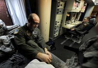 2nd Lt. Kameron Kantor, 742nd Missile Squadron intercontinental ballistic missile combat crew deputy, removes his boots as 1st Lt. Kris Riedman, 742nd MS ICBM crew commander answers the phone in the launch capsule of the Oscar 1 missile alert facility near Mohall, N.D., Jan. 9, 2015. While stationed in the capsule, Riedman and Kantor work 24 hours a day; eating, sleeping in shifts, and even using a bathroom, all while inside the capsule. (U.S. Air Force photo/Senior Airman Stephanie Morris)