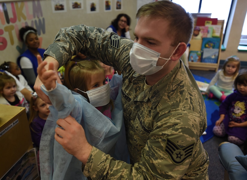 Staff Sgt. David Brockes, 779th Dental Squadron dental assistant, dresses Jade Hall into scrubs at the Child Development Center during a demonstration for National Children’s Dental Health Month on Joint Base Andrews, Md., Feb. 26, 2015. The hygienists played a game highlighting foods that encouraged good dental hygiene. (U.S. Air Force photo/ Senior Airman Nesha Humes)