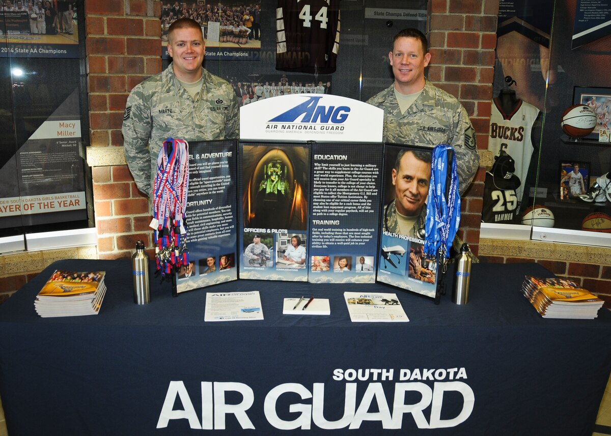 SIOUX FALLS, S.D. - Master Sgt. Eric Tidemann and Tech. Sgt. Bo Martz, 114th Force Support Squadron recruiters, stand post at their booth during military appreciation day at the Northern Sun Intercollegiate Conference NCAA II basketball tournament in Sioux Falls, S.D., March 1, 2015. The pair gave away lanyards, water bottles, flash drives, and basketballs to kids and fans at the event.(National Guard photo by Staff Sgt. Luke Olson/Released) 