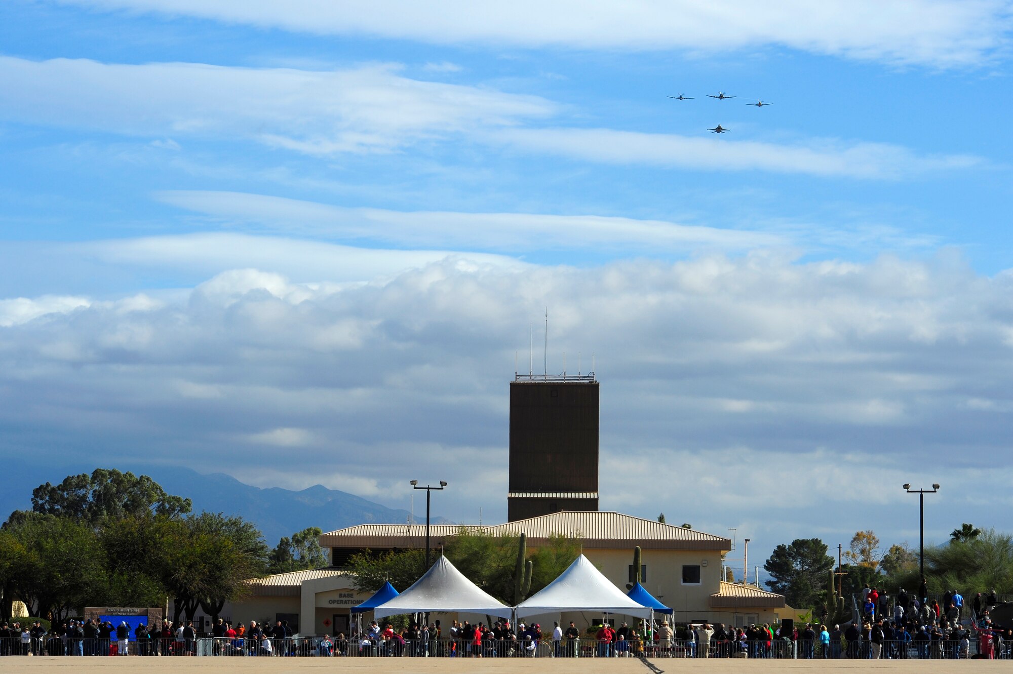Spectators watch as a P-47 Thunderbolt, two P-51 Mustangs, and a F-16 Fighting Falcon fly in formation overhead during the 2015 Heritage Flight Training and Certification Course at Davis-Monthan Air Force Base, Ariz., Feb. 28, 2015. During the course, aircrews practiced ground and flight training to enable civilian pilots of historic military aircraft and U.S. Air Force pilots of current fighter aircraft to fly safely in formations together. (U.S. Air Force photo by Staff Sgt. Courtney Richardson/Released)
