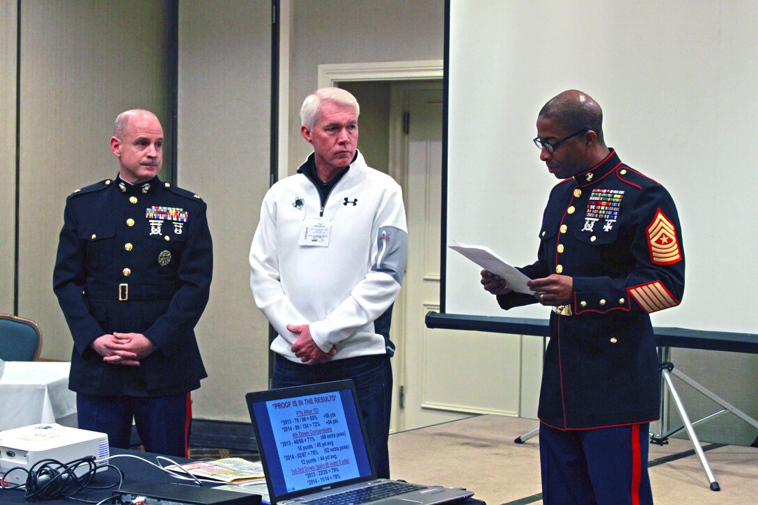 U.S. Marine Sgt. Maj. Troy A. Nicks (right) reads a biography of Hal Wasson (center), head football coach of Southlake Carroll High School and recipient of the 2015 Semper Fidelis Award during a Glazier Football Clinic hosted at the Sheraton DFW Airport Hotel, Irving, Texas, Feb. 28. Wasson lead his football program to a Class 5A-I state championship in 2011. (Official Marine Corps photo by Sgt. Alfredo Ferrer)
