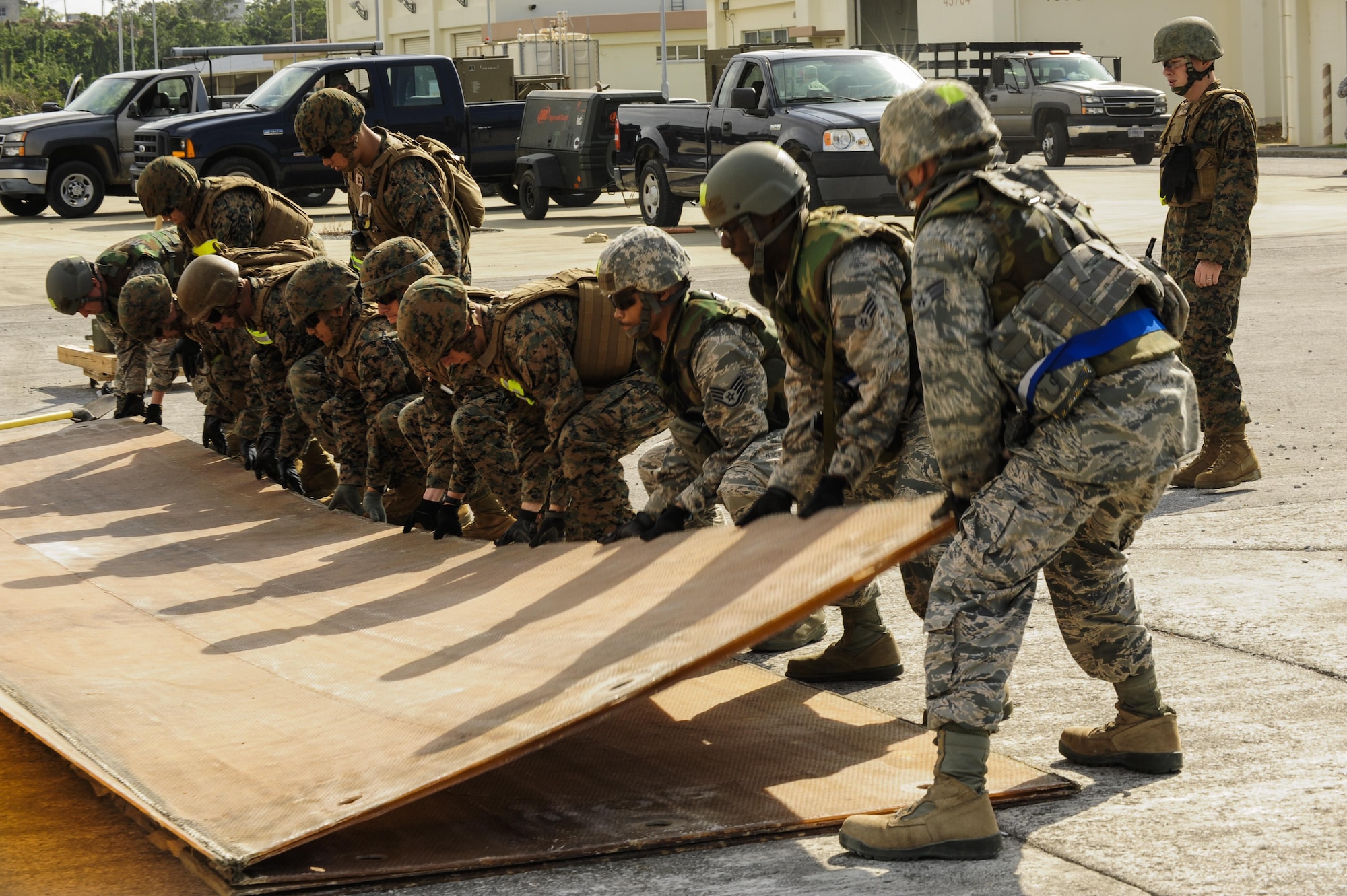 Airmen from the 18th Civil Engineer Group and 172nd and 171st Engineering Company Marines unfold a fiber glass mat during a joint airfield damage and repair contingency exercise Feb. 26, 2015, at Kadena Air Base, Japan. The Airmen and Marines worked together in order to repair a 50-foot crater on a mock runway. (U.S. Air Force photo/Airman 1st Class John Linzmeier)
