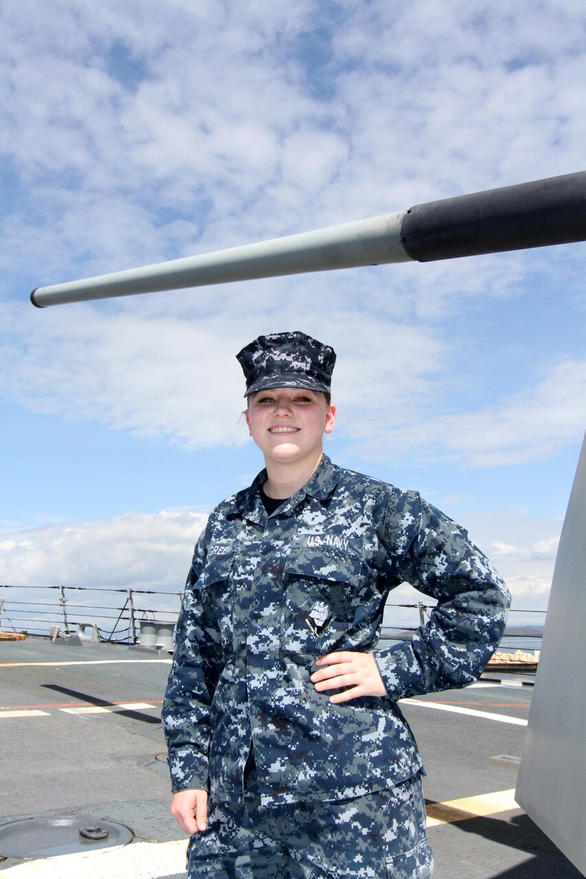 Navy Seaman Morgan Pilgreen stands in front of the MK45 5-inch, .62-caliber gun aboard the USS Jason Dunham during a port visit to Guantanamo Bay, Cuba, Feb. 7, 2015. U.S. Army photo by Sgt. Richard Hoppe