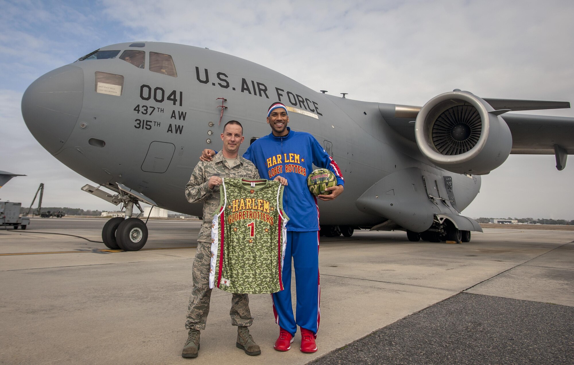 Tech. Sgt. Jeffrey Landis, 315th Maintenance Squadron, Hold up his new Harlem Globetrotter jersey with Globetrotter "Zeus" McClurkin outside a C-17 Globemaster III earlier this week. Landis was selected as the Globetrotters' Hometown Hero for their March 10 game in North Charleston. (U.S. Air Force Photo by Senior Airman Thomas Brading)
