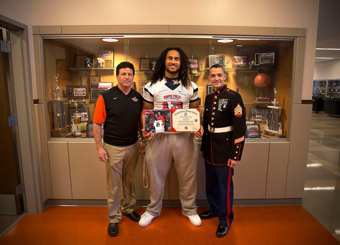 Sgt. Daniel Pluth (right), a Marine recruiter in Tacoma, Washington, presents a Semper Fidelis All-American Bowl certificate to Benning Potoae (center), a senior at Lakes High School in Lakewood, Washington, together with Lakes football coach Dave Miller March 3, 2015. Potoae, a highly-touted defensive end from Dupont, Washington, was one of three Washington State football players selected to play in the Jan. 4 game in Carson, California. Following his high school graduation, Potoae will attend the University of Washington on a football scholarship. (U.S. Marine Corps photo by Sgt. Reece Lodder)