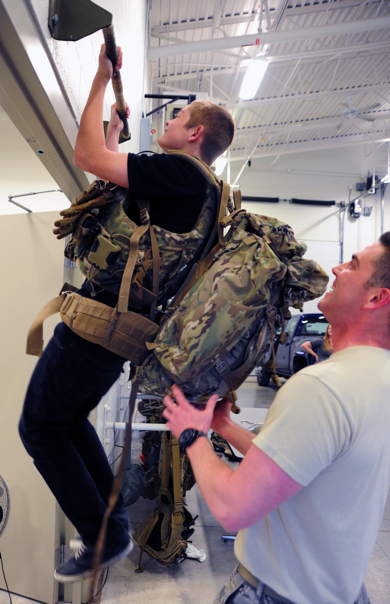 Senior Airman Robert Sutton, 509th Civil Engineer Squadron explosive ordinance disposal technician, assists Gage Baska, a 14 year-old resident of Blue Springs, Mo., as he does pull-ups while wearing 20 pounds of protective gear at Whiteman Air Force Base, Mo., Nov. 5, 2014. As part of Baska’s intervention program, he had an opportunity to experience what it’s like to work out as an EOD technician. (U.S. Air Force photo by Staff Sgt. Nick Wilson/Released)