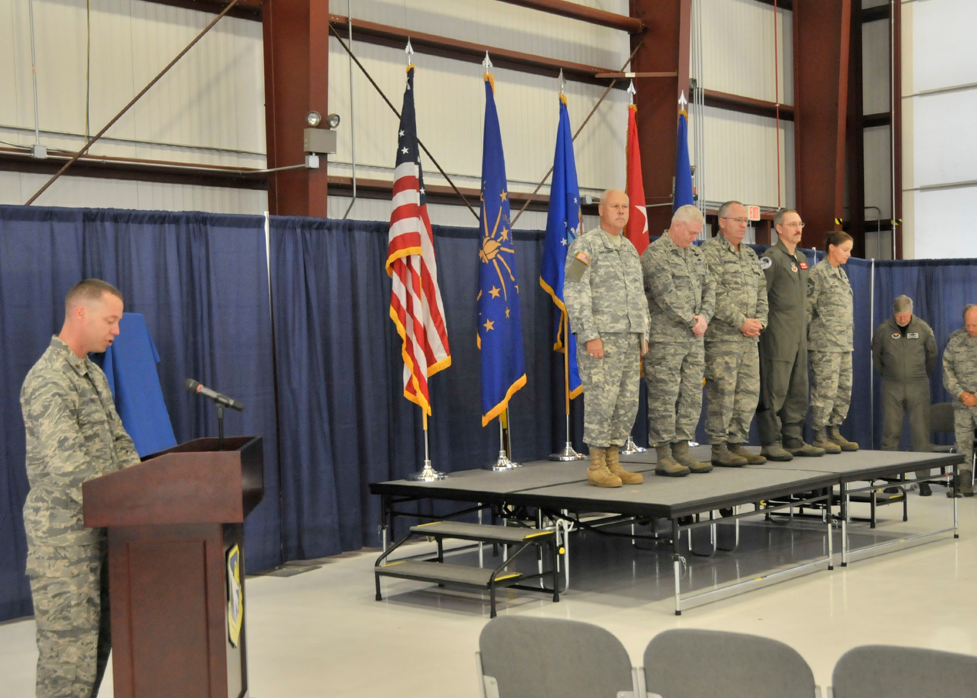 Maj. Michael Frese (left), Chaplain of the 122nd Fighter Wing, opens the wing’s change of command ceremony with a prayer, Sep. 13, 2014, Fort Wayne Air National Guard Base, Fort Wayne, Indiana. Standing from left to right on stage is Maj. Gen. R. Martin Umbarger, the Adjutant General of Indiana, Brig. Gen. Jeffrey W. Hauser, Assistant Adjutant General of Indiana, Col. David L. Augustine, retiring 122FW commander, Col. Patrick R. Renwick, newly appointed 122FW Commander, and Chief Master Sgt. Christine A. Hutchins, Command Chief of the 122FW. (Air National Guard photo by Senior Airman Joseph Boals/Released)