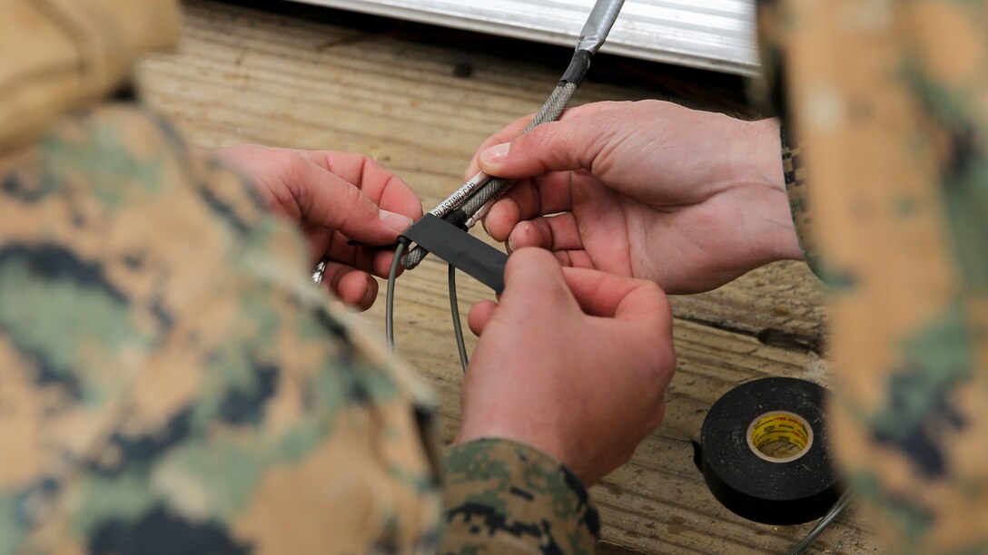 A Marine with Mobility Assault Company, 2nd Combat Engineer Battalion, 2nd Marine Division tapes two blasting caps to the Det Linear that is attached to the door during an urban breaching course aboard Camp Lejeune, N.C., March 3, 2015. A Det Linear is three, eight-foot sections of detonation cord taped together and taped either at the center, left or right side of the door. (U.S. Marine Corps photo by Cpl. Justin T. Updegraff)