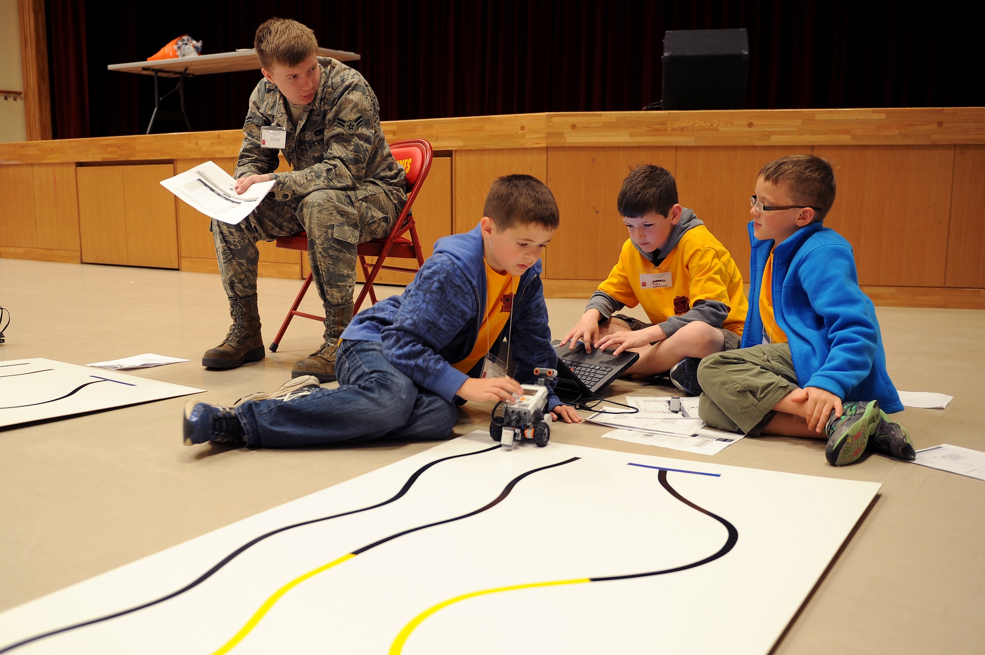 U.S. Air Force Airman 1st Class Thomas McCalister, 18th Component Maintenance Squadron aerospace propulsion technician, judges Stearley Heights Elementary School students on their ability to program a robot to follow lines of different colors during an island-wide robotics competition on U.S. Marine Corps Camp Foster, Japan, Feb. 20, 2015. Service members from around the island acted as judges for the competition, which tested the ability of Department of Defense dependent elementary, middle and high school students to program robots to perform various tasks. (U.S. Air Force photo by Airman 1st Class Zade C. Vadnais)