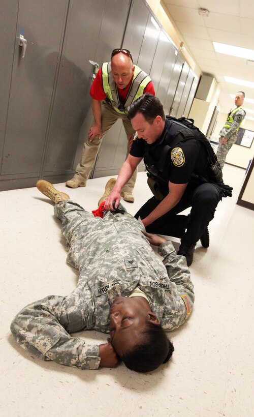 Hoover, Ala., Police officer Zack Falkner acts out the role of applying care to a simulated wound on the leg of Spc. Jacqueline Thompson, a human resources specialist with the 87th U.S. Army Reserve Support Command (East), while Lt. Charles McDonald, also with the Hoover Police Department, looks on. The Hoover PD was participating in an exercise with members of the 87th USARC(E) to provide training on responding to an active shooter situation. (U.S. Army photo by Sgt. 1st Class Ryan C. Matson, U.S. Army Reserve Support Command (East))