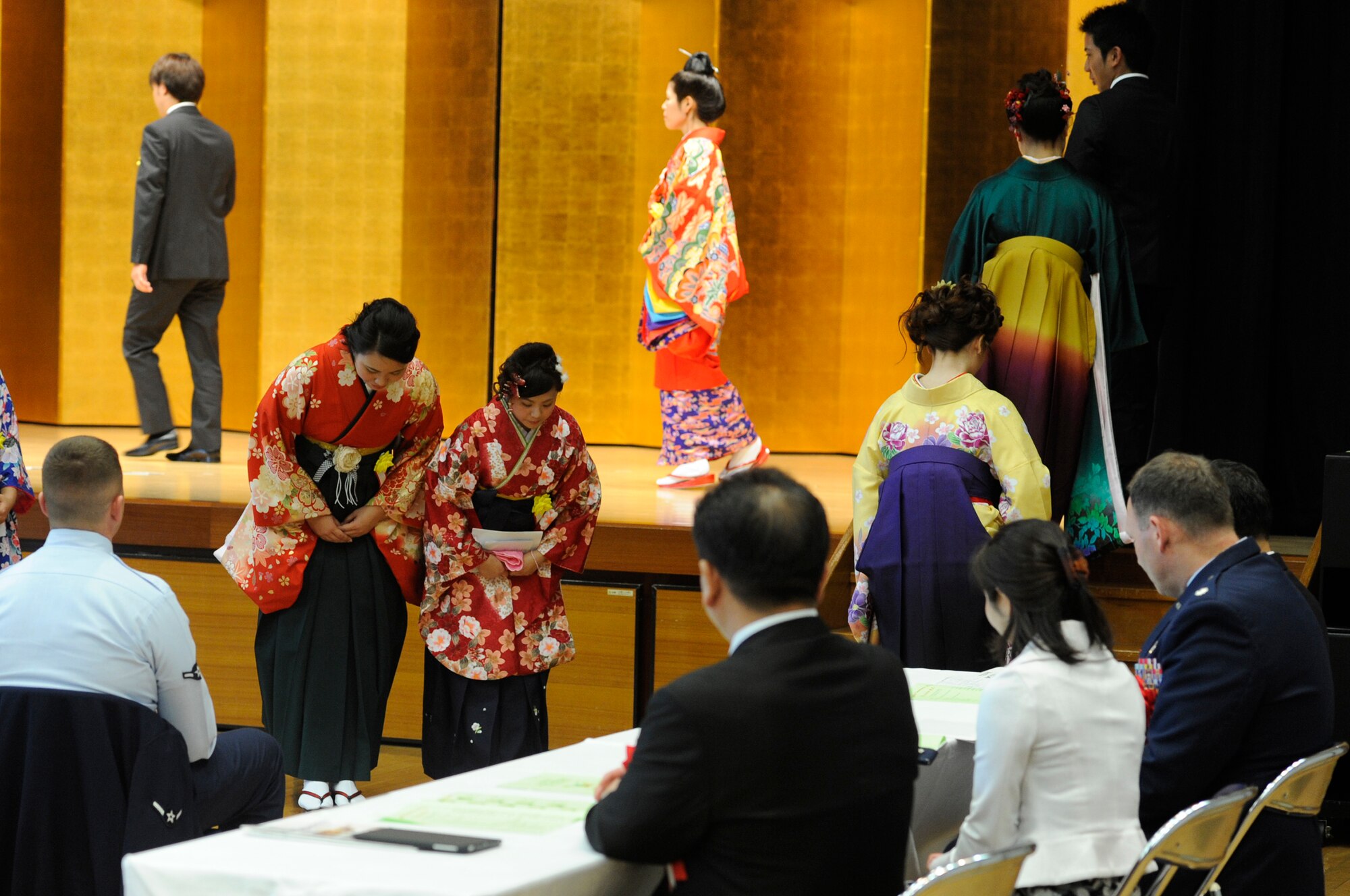 Graduates from the Kadena Language Institute class of 2015 show their respect to distinguished guests by bowing to their table before heading onto the stage at the Rotary Plaza in Kadena Town, Japan, March 6, 2015. The KLI is a two-year vocational school which included a four-week internship at Kadena Air Base, Japan, where they practiced speaking English and working with customers. (U.S. Air Force photo by Staff Sgt. Marcus Morris)
