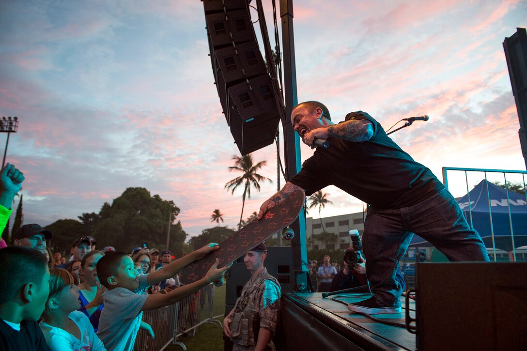 Actor Jason “Wee Man” Acuna, gives a skateboard to an audience member on stage during a USO concert for service members and their families on Joint Base Pearl Harbor–Hickam, Hawaii, March 8, 2015.