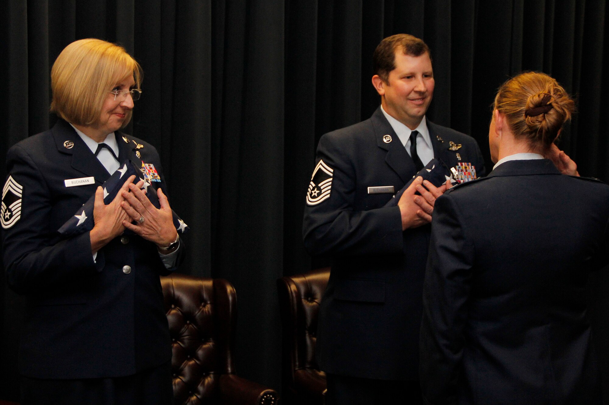 PETERSON AIR FORCE BASE, Colo. – Chief Master Sgt. Debbie Buchanan, 34th Aeromedical Evacuation Squadron superintendent and Senior Master Sgt. Rick Buchanan, 302nd Aeromedical Staging Squadron medical readiness superintendent, who are husband and wife, receive American Flags during their joint retirement ceremony Dec. 6, 2014, here. The Buchanans spent the majority of their 52 years of combined service as aeromedical technicians with assignments in the Air Force, Air National Guard and Air Force Reserve. They were two of  the first  members of the Peterson-based aeromedical evacuation squadron and were instrumental in building the 34th AES which stood up here in March 2008.  Prior to their Air Force Reserve assignments with the 302nd Airlift Wing, both were assigned as aeromedical evacuation technicians in the Oklahoma Air National Guard where they provided medical response to the April 1995 bombing victims of the Alfred P. Murrah Federal Building in downtown Oklahoma City. The Buchanans were both awarded the Meritorious Service Medal during the ceremony. 