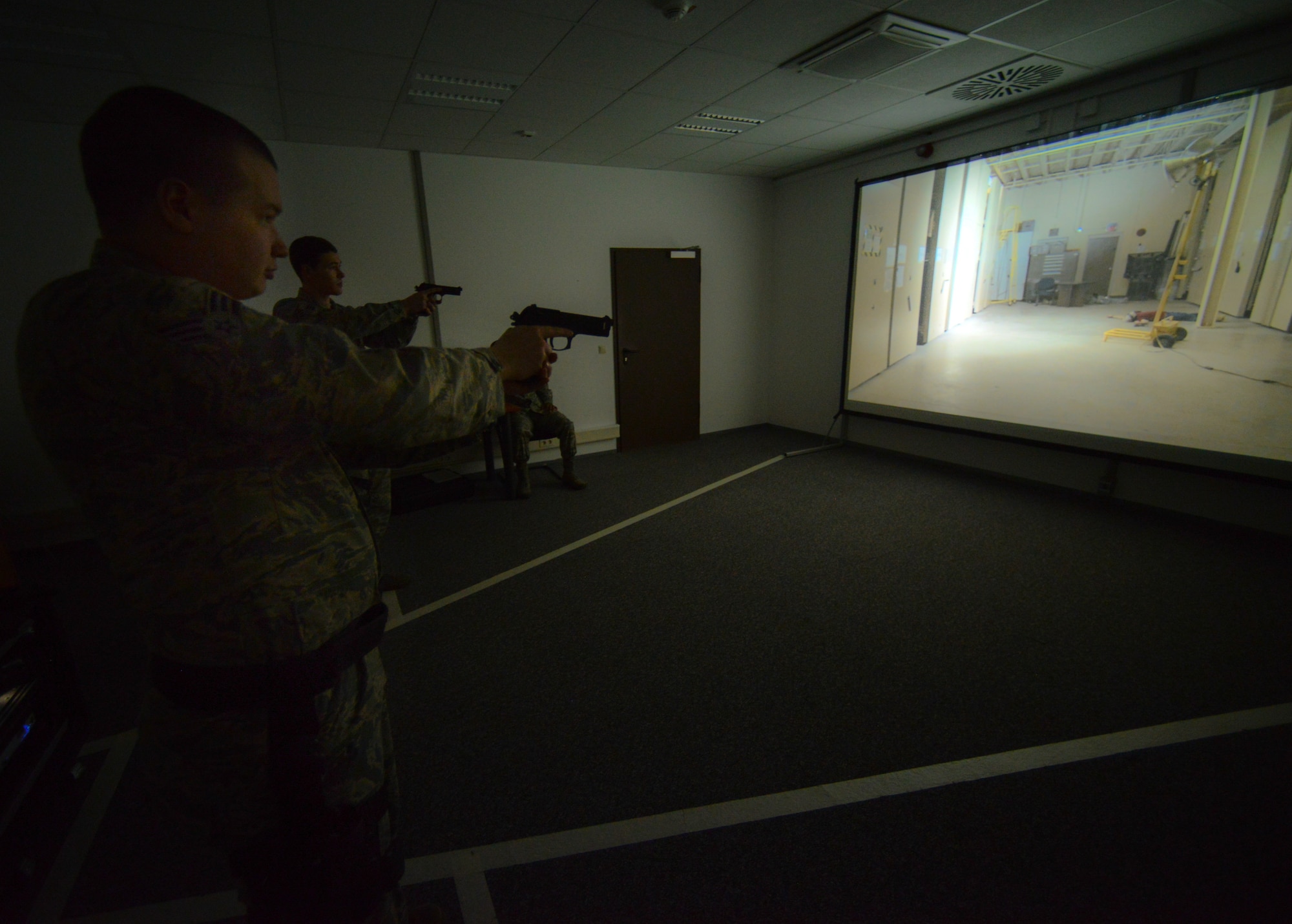 Airmen assigned to the 86th Security Forces Squadron react to a scenario during a firearms training system exercise at Ramstein Air Base, Germany, March 6, 2015.  The Air Force-wide system allows law enforcement a virtual experience with the use of laser-pointed air-compressed weapons on a training system similar to an interactive video game. (U.S. Air Force photo/Senior Airman Nicole Sikorski)