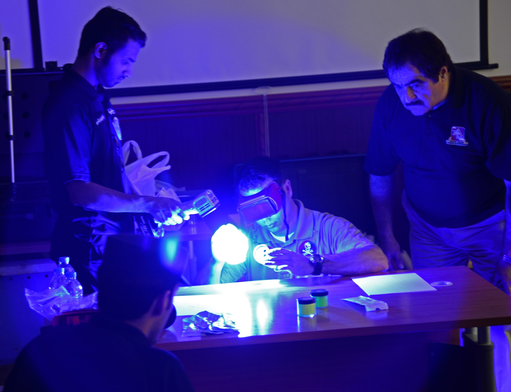 U.S. Special Agent Chad Hutchins, center, Forensics Science Consultant from the Federal Law Enforcement Training Center in Brunswick, Ga., looks at a can which he dusted with neon fingerprint powder to enhance a fingerprint during a liaison exchange, March 3, 2015, at the Criminal Evidence and Information Department, Ar-Rayyan, Qatar.  During the liaison exchange, members from Air Force Office of Special Investigations Detachment 241 and their Qatari counterparts exchanged different forensic methods they use when investigating a crime scene. Fingerprint powders have various formulations, and the appropriate powder must be used on the appropriate surface. For example, dark colored powders will show up a fingerprint far better on a light surface. (U.S. Air Force photo by Senior Airman Kia Atkins)