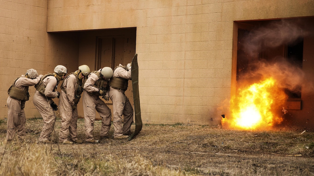 Marines with 2nd Explosive Ordnance Disposal Company, 8th Engineer Support Battalion stand in a line behind a shielding blanket as an explosive charge detonates during a dynamic entry sustainment course at a Military Operations in Urban Terrain exercise aboard Camp Lejeune, N.C., March 9, 2015.  Explosive charges were used to shatter and open doors for quick entry into a secure space, while maintaining the element of surprise.