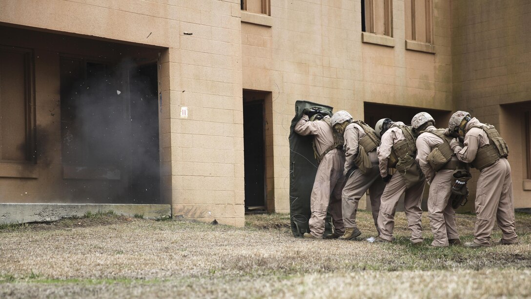 Marines with 2nd Explosive Ordnance Disposal Company, 8th Engineer Support Battalion stand in a line behind a shielding blanket as an explosive charge detonates during a dynamic entry sustainment course at a Military Operations in Urban Terrain exercise aboard Camp Lejeune, N.C., March 9, 2015.  Explosive charges were used to shatter and open doors for quick entry into a secure space, while maintaining the element of surprise. 