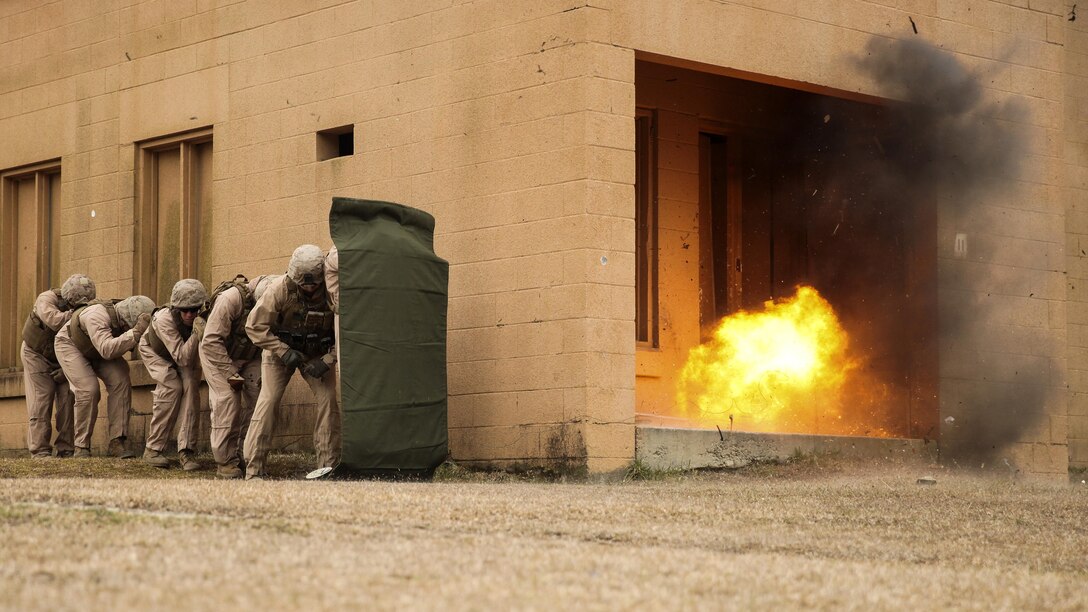 Marines with 2nd Explosive Ordnance Disposal Company, 8th Engineer Support Battalion stand in a line behind a shielding blanket as an explosive charge detonates during a dynamic entry sustainment course at a Military Operations in Urban Terrain exercise aboard Camp Lejeune, N.C., March 9, 2015.  Explosive charges were used to shatter and open doors for quick entry into a secure space, while maintaining the element of surprise. 