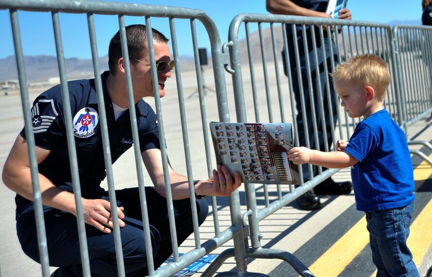 Master Sgt. Pete Spoelstra, U.S. Air Force Air Demonstration Squadron Thunderbirds production superintendent, gives Justin Roberts, 2, a signed Thunderbird team booklet during Indian Springs Appreciation Day March 10, 2015 at Creech Air Force Base, Nevada. The team performs precision aerial maneuvers to exhibit the capabilities of modern high-performance aircraft to audiences throughout the world. (U.S. Air Force photo by Airman 1st Class Christian Clausen/Released) 