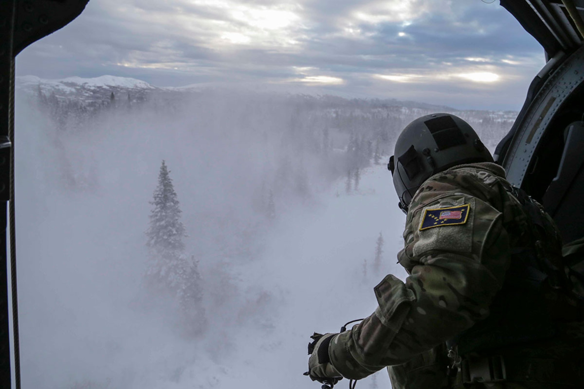 Alaska Air National Guard Staff Sgt. Jheren Svoboda, a flight engineer with the 210th Rescue Squadron,  prepares to hoist a combat rescue officer out of an HH-60 Pave Hawk helicopter during a training mission near Mount Susitna Dec. 16. (U.S. Army National Guard photo by Sgt. Balinda O’Neal)