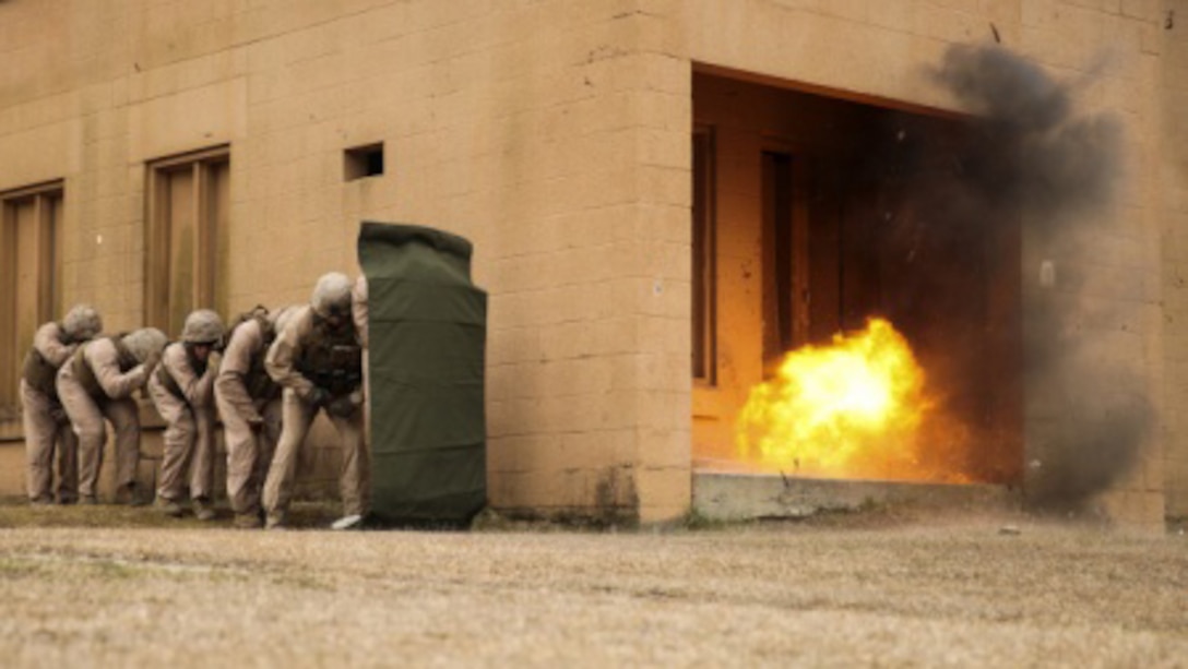 Marines with 2nd Explosive Ordnance Disposal Company, 8th Engineer Support Battalion stand in a line behind a shielding blanket as an explosive charge detonates during a dynamic entry sustainment course at a Military Operations in Urban Terrain exercise aboard Marine Corps Base Camp Lejeune, North Carolina, March 9, 2015. Explosive charges were used to shatter and open doors for quick entry into a secure space, while maintaining the element of surprise.
