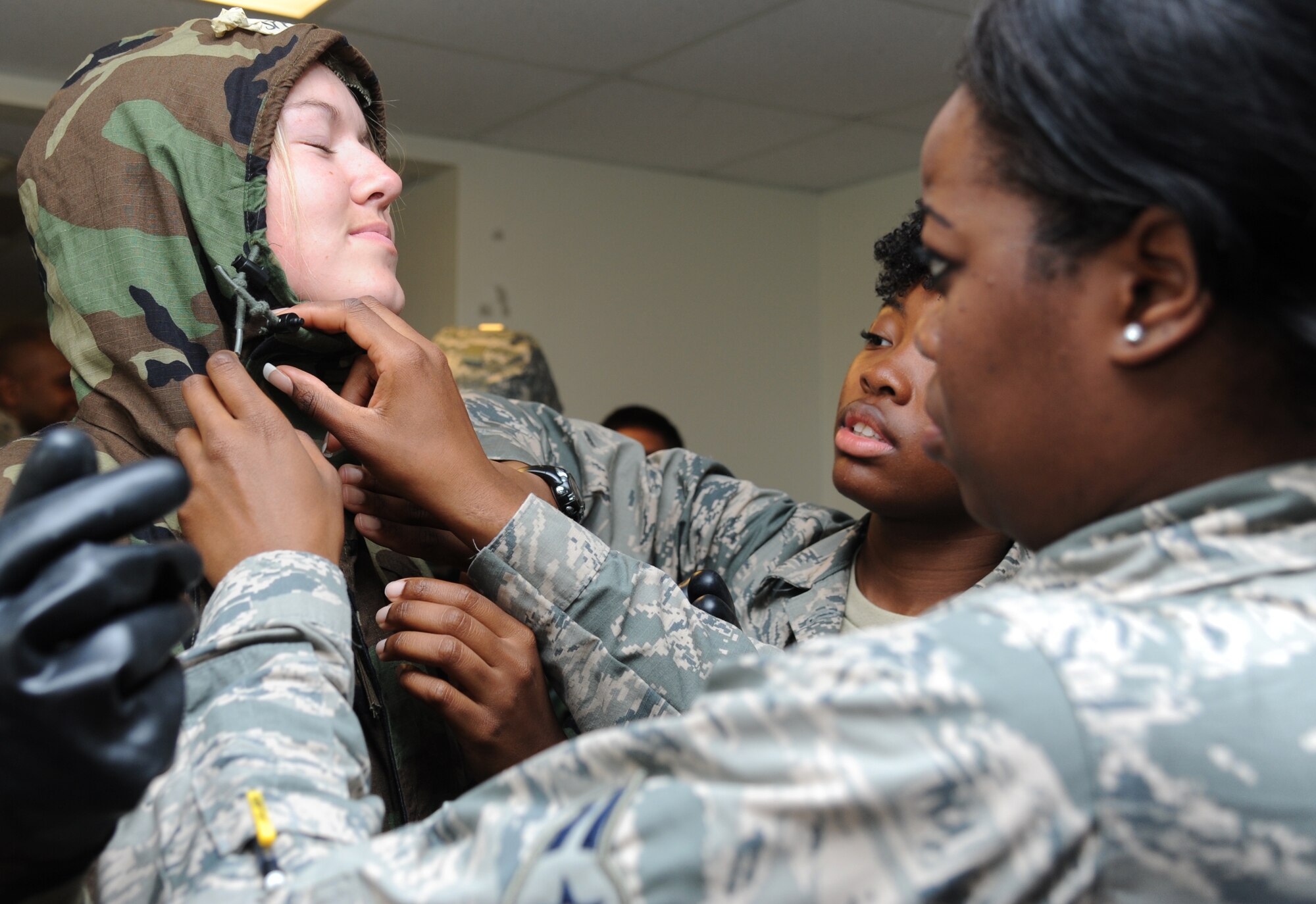 Airman 1st Class Raechel Oyen, Airman Nasia Brown and Airman 1st Class Camerae Lang, 335th Training Squadron students, utilize the “buddy system” to secure chemical warfare gear on Oyen during an “Introduction to Mobility” training day for non-prior service Airmen March 13, 2015, at Keesler Air Force Base, Miss.  Airmen participated in pre-deployment training scenarios such as: going through a mobility processing line, administering self-aid and buddy care, reviewing the steps for chemical warfare gear and receiving a pre-deployment briefing.  The training was conducted to better prepare Keesler’s Airmen for deployment operations.  (U.S. Air Force photo by Kemberly Groue)