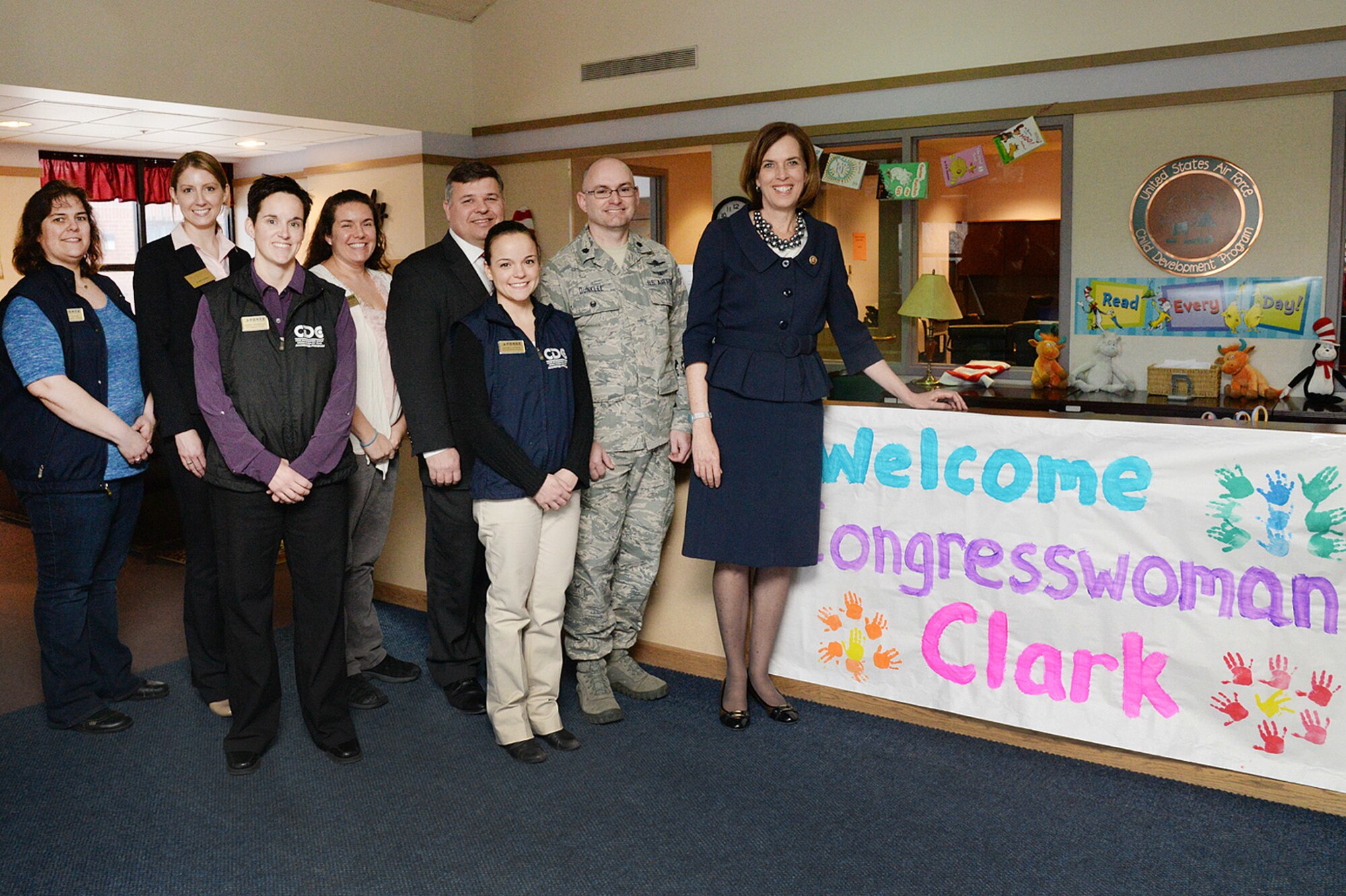 U.S. Rep. Katherine Clark stands in front of a welcome sign in the Child Development Center lobby with caregivers and base senior leaders here, March 12. During her visit, Clark met with the CDC staff to discuss military child care and related topics during her visit and read to several groups of children. (U.S. Air Force photo by Linda LaBonte Britt)  
